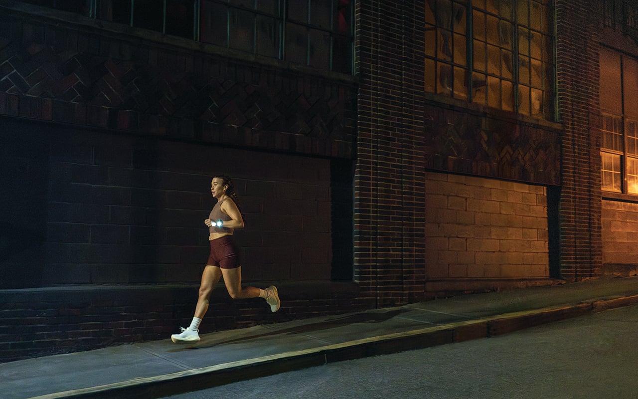 一名女子在黑暗中跑步,並開啟 Garmin 智能手錶的手電筒功能。